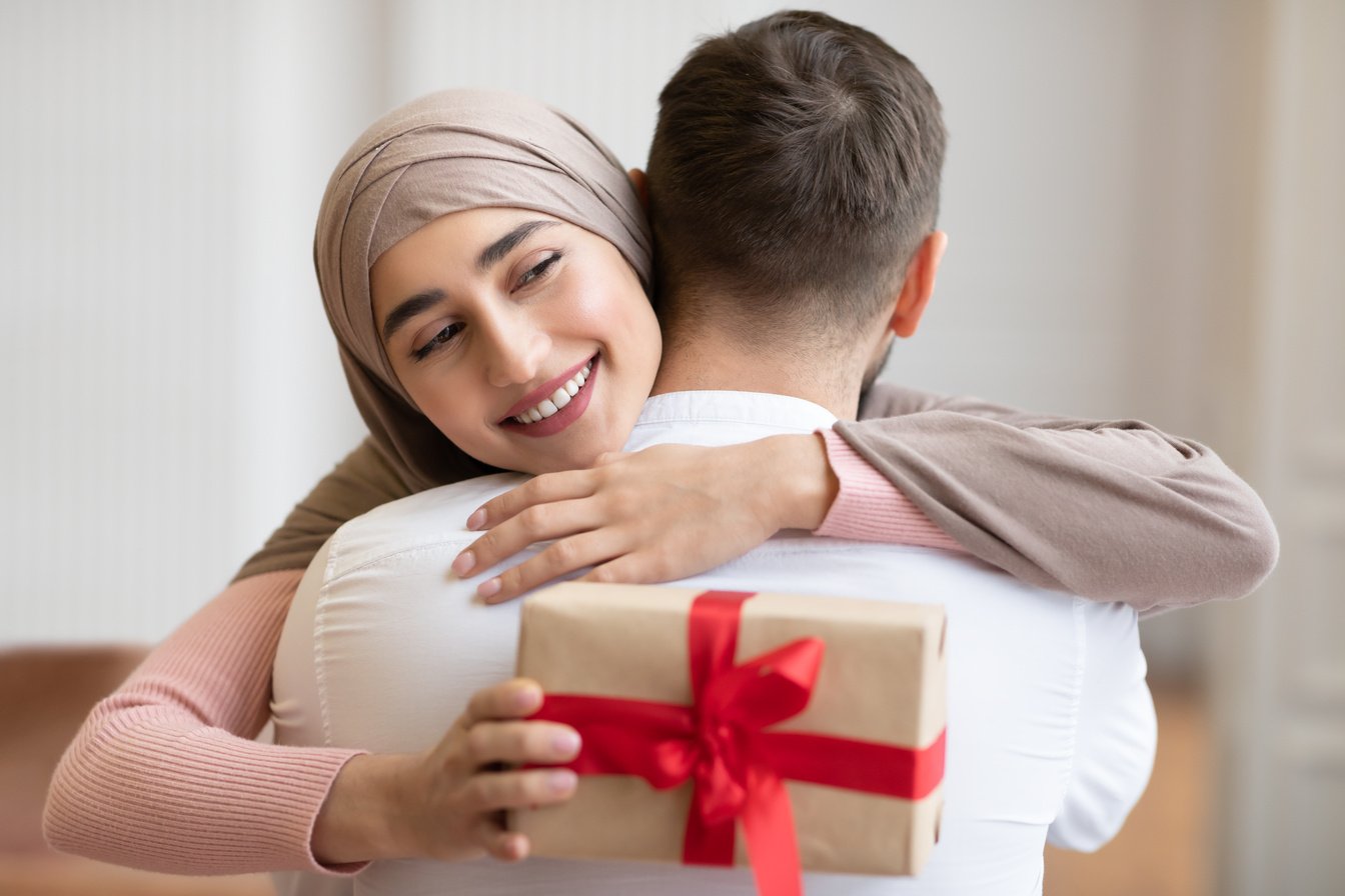 Joyful Muslim Wife Embracing Husband Holding Birthday Gift At Home